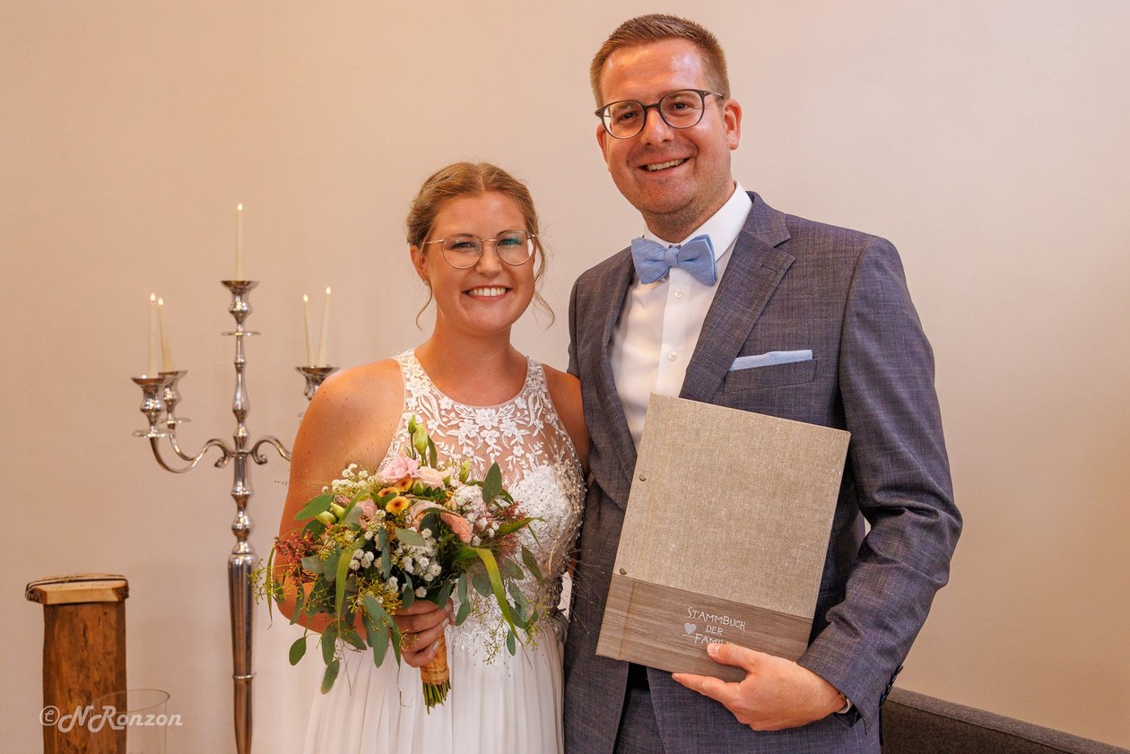 Ein strahlendes Brautpaar Alina und Fabian mit Stammbuch und Blumenstrauß am ende der Trauung.